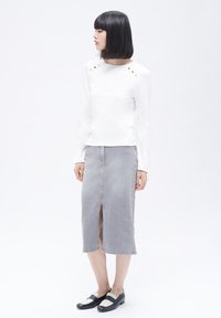 Blusa blanca de manga larga con cuello redondo y tres botones decorativos dorados. Falda midi de mezclilla gris claro con una abertura frontal, combinada con zapatos negros.