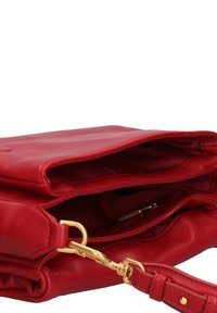Le sac à main en cuir rouge présente une texture lisse, une poche zippée et des accents en métal doré, avec une bandoulière amovible pour plus de polyvalence.