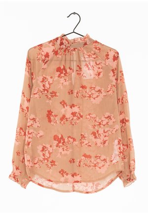 Blouse longue transparente à manches longues avec col montant et poignets à volants, à motif floral rose et rouge sur tissu beige, suspendue sur un cintre noir.