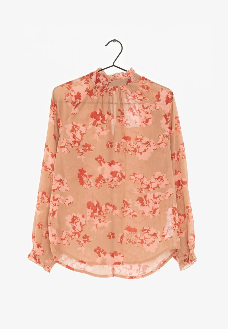Blouse longue transparente à manches longues avec col montant et poignets à volants, à motif floral rose et rouge sur tissu beige, suspendue sur un cintre noir.