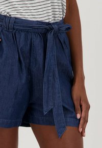 Pantalones cortos de lino azul marino con un cinturón atado en la cintura, que presentan un corte holgado y una tela texturizada, vistos de la cintura hacia abajo.