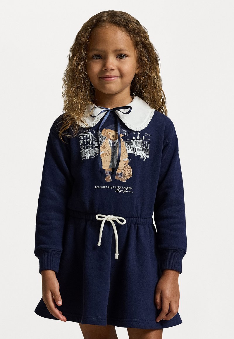 Temno modra obleka s svobodnimi rokavi, bela Peter Pan ovratnik, pas s vrvico in grafika medveda v plašču; material iz bombažne mešanice.