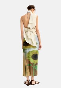 Plisowana midi spódnica z nadrukiem słonecznika, wykonana z lekkiego materiału. Górna część związana jest kremowym szalikiem.