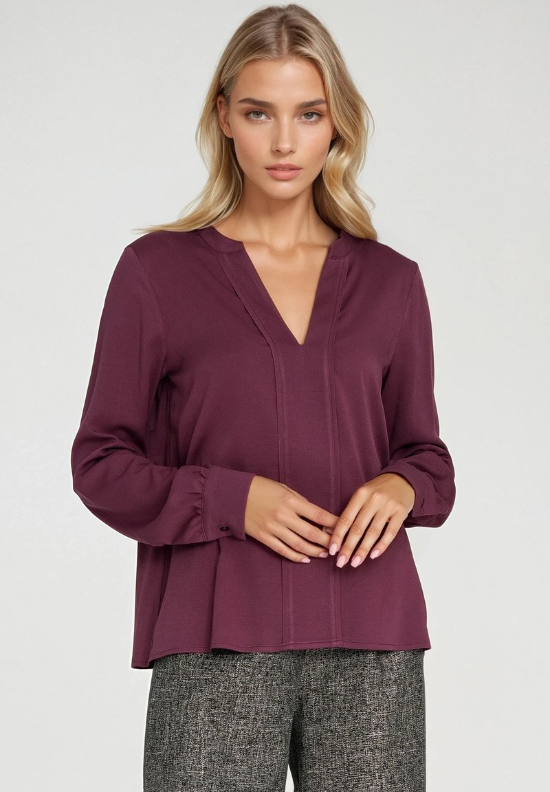 Bordowa bluzka z długim rękawem i dekoltem w serek, z pionowymi szwami i marszczonymi mankietami. Gładka tekstura, luźny krój, dobrze komponuje się z wzorzystymi spodniami.