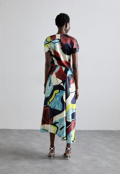 Rochie maxi colorată, cu model, dintr-un material neted; are mâneci scurte, o siluetă fluidă și o linie asimetrică a tivului. Este purtată cu sandale cu toc înalt.