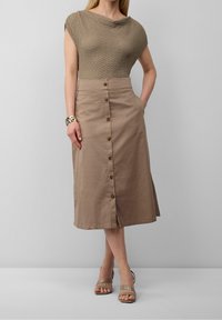 Maglione beige con un motivo testurizzato, abbinato a una gonna leggera color marrone chiaro di lunghezza al ginocchio con chiusura a bottoni frontali e tasche laterali.