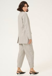 Vaaleanharmaa pinstripe-puku, jossa on muotoiltu takki ja kapenevat housut, takana halkio, ja yhdistetty mustiin, korkokenkäisiin slingback-kenkiin.