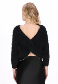Zwarte, harige trui met lange mouwen, een diepe V-achterkant en een geschulpte zoom. Bevat metalen accenten langs de randen.