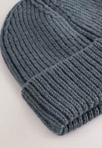 Pletena kapa tamnoplave boje s okomitim rebrastim uzorkom i uvrnutim rubom. Izrađena od mekanog, debelog prediva za toplinu i udobnost.