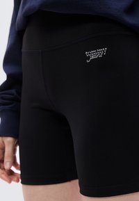 Μαύρο αθλητικό σ ορτς από λείο, ελαστικό ύφασμα με εφαρμοστή σχεδίαση. Διαθέτει ασημένιο λογότυπο «tommy jeans» στο μπροστινό μέρος.