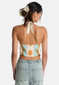 Μπλούζα κοντή με σφηκοφωλιά και πολύχρωμα σχέδια σε πορτοκαλί, μπλε και άσπρο· διαθέτει δέσιμο στο λαιμό τύπου halter και υφή στο ύφασμα.