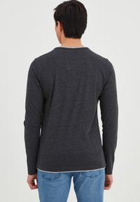 Langærmet grå skjorte i blødt stof med rund hals og kontrastfuld lysegrå kant, parret med blå jeans.