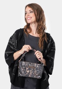 Bolso de mano a rayas negras y beige con una cadena de asa, que presenta una textura ondulada y un logo. La modelo sostiene el bolso mientras viste un atuendo negro.