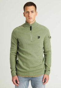 Olivgrüner Pullover, hoher Kragen, Reißverschluss, gerippte Bündchen und Saum, kleines schwarzes Logo-Patch auf der Brust, strukturiertes Strickmaterial.