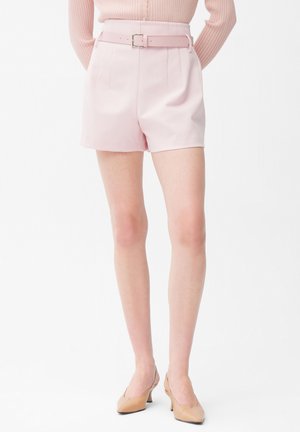 Kvinde iført lyserøde skræddersyede shorts med høj talje og bælte, kombineret med nude kitten heel-sko og en lyserød ribstrikket langærmet top.