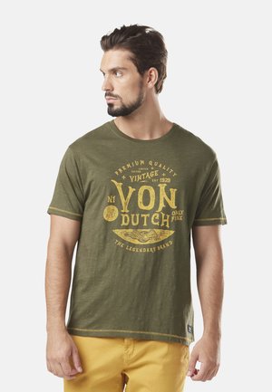 T-shirt verte en tissu texturé avec un design graphique jaune, comportant le nom de la marque et l'année de création, col rond, manches courtes.