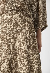 Tessuto marrone e beige con motivo, finitura testurizzata, caratterizzato da una parte superiore a vestibilità ampia e una gonna fluida, che mette in mostra cuciture e polsini visibili.