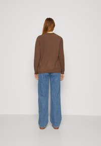 Maglia marrone a maniche lunghe abbinata a jeans blu larghi. Il tessuto sembra morbido, con un design semplice e un classico colletto rotondo.