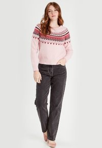 Jasnoróżowy sweter dziany z wzorzystą karczkiem z czerwonymi i białymi wzorami, w zestawie z ciemnoszarymi dżinsami i miękkimi różowymi butami.
