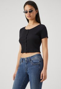 Svart kortärmad topp med knappstängning och subtil "GAP"-logotyp. Kombineras med blå denimjeans. Slät textur.