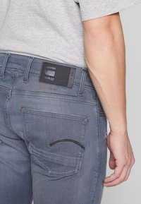 Grå denimjeans har en läderlapp med präglad logotyp, femficksdesign och subtila sömdetaljer. Slät yta.