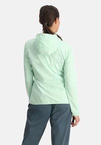 Giacca verde menta chiaro con cappuccio, caratterizzata da un motivo testurizzato, design aderente e maniche lunghe. Indossata con pantaloni blu scuro.