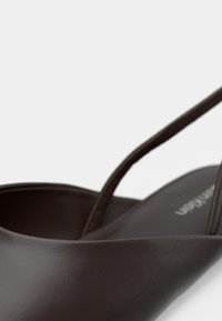 Hnědá kožená bota s elegantním, zakřiveným designem a tenkými pásky. Vyznačuje se hladkým povrchem a minimalistickou estetikou.