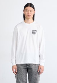 Tricou alb cu mâneci lungi, având text grafic negru pe piept, asortat cu blugi gri decolorati. Croială casual, material din bumbac.