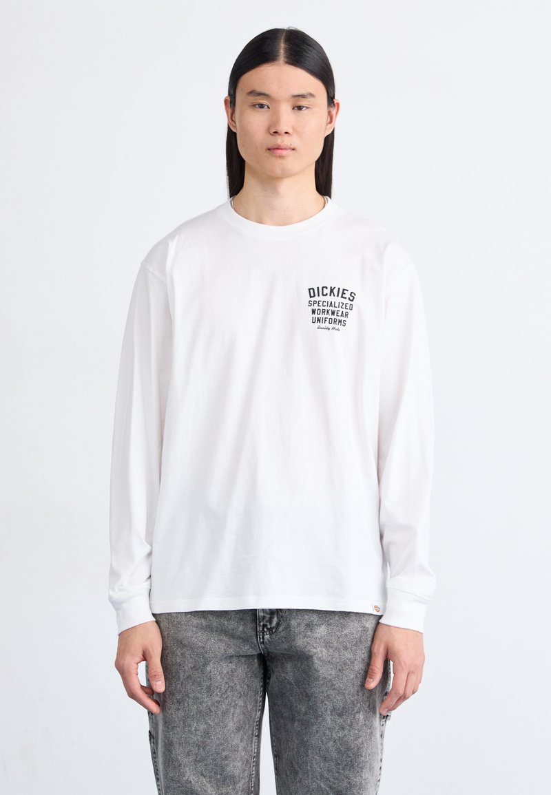 Tricou alb cu mâneci lungi, având text grafic negru pe piept, asortat cu blugi gri decolorati. Croială casual, material din bumbac.
