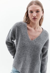 Maglione grigio a coste con scollatura a V profonda, maniche lunghe, vestibilità comoda e tessuto testurizzato. Notevole motivo diagonale sul davanti.