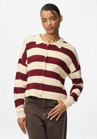 Svītrains kardigans krēmkrāsā un burgundijas tonī ar apkakli, priekšējām pogām un vaļēju piegriezumu. Adīts ar garām piedurknēm un ribotu apdari piedurkņu galiem.