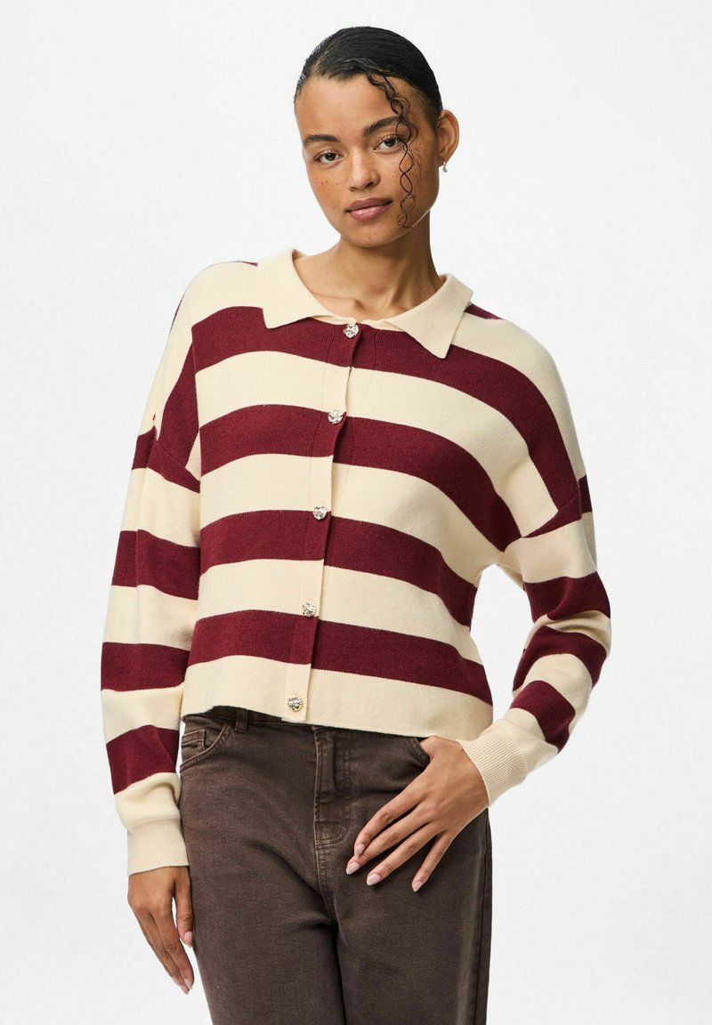 Svītrains kardigans krēmkrāsā un burgundijas tonī ar apkakli, priekšējām pogām un vaļēju piegriezumu. Adīts ar garām piedurknēm un ribotu apdari piedurkņu galiem.