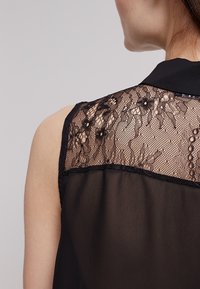 Sort ærmeløs top med en blonde ryg med blomsterprint og små detaljer, blødt stof med en gennemsigtig finish.