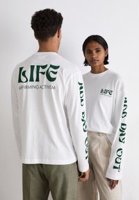 Weiße Langarm-T-Shirts mit grünen Grafiken, auf denen auf dem Rücken "LIFE" und "AFFIRMING ACTIVISM" sowie "DAY OUT" entlang der Ärmel steht.