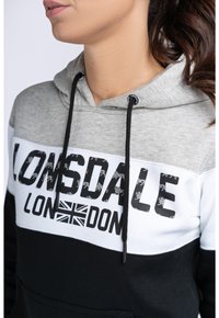 Grå, vit och svart hoodie med en kenguruficka. Har tydlig text "Lonsdale London" och ett mönster av Union Jack på framsidan.