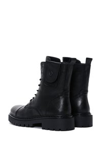 Un par de botas de combate de cuero negro con cordones, suelas gruesas y bolsillos con tapa de botón a presión en los laterales.