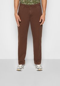 Bruna rakbenade byxor med knappstängning, tillverkade av bomull, med sidofickor och en avslappnad passform, som är kombinerade med grå och vita sneakers.