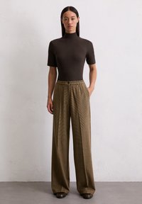 Bruin aansluitend topje met korte mouwen en een hoge hals, gecombineerd met brede geruite broek in bruin- en groentinten. Glad materiaal met een relaxte fit.
