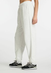 Hellgraue Sweatpants mit einem elastischen Bund, seitlichen Taschen und gerippten Säumen, kombiniert mit schwarzen Turnschuhen mit grauen und weißen Akzenten.