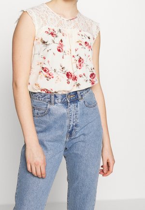 Blusa floreale con yoke in pizzo, morbido tessuto crema, rose rosa e rosse, vestibilità ampia, abbinata a jeans in denim azzurri a vita alta.