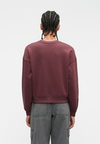 Burgundy sweatshirt with a ribbed crew neckline, dropped shoulders, and textured fabric, paired with gray cargo pants featuring side pockets.