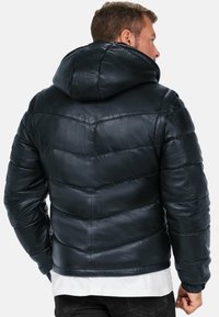 Giacca puffer in pelle blu scuro con cappuccio, dotata di sezioni trapuntate, una texture liscia e polsini elastici. Accentuata da una lieve lucentezza.