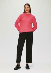 Helle rosa Strickjacke mit gerippter Textur und dreieckigem Ausschnittmuster, kombiniert mit schwarzen geraden Hosen und glänzenden Schuhen.