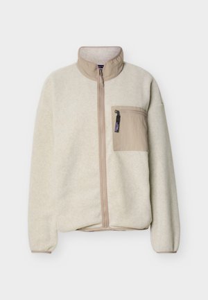 Μπεζ φλις μπουφάν με πλήρες φερμουάρ, ψηλό γιακά και τσεπάκι στο στήθος με φερμουάρ, παρουσιάζεται πάνω σε απλό ανοιχτό φόντο.