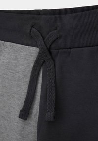 Pantalons de survêtement en tissu gris et bleu marine foncé présentant une taille texturée, des couleurs contrastées et un cordon tressé pour l'ajustement.