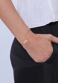 Bracelet en chaîne dorée avec un charme arc-en-ciel en émail multicolore, présentant des rayures rouges, orange, jaunes, vertes, bleues et violettes.