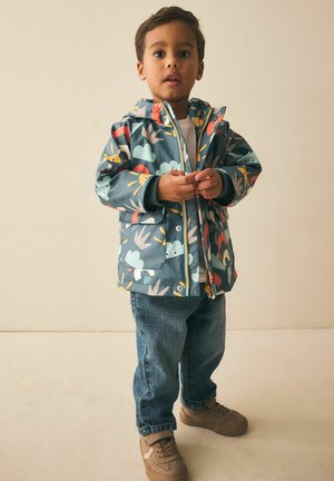 Vattentät jacka med en blågrön bas och färgglada mönster av djur och natur, dragkedja och fodrad huva. Kombinerad med jeans.