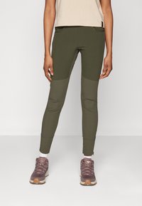 Olive green leggings featuring textured panels at the knees. Paired with a beige top and purple footwear with a rugged sole.