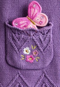 Lila gestrickter Stoff mit einer Tasche, die mit floraler Stickerei verziert ist. Ein rosa und pfirsichfarbenes, gesticktes Schmetterling sitzt in der Tasche.
