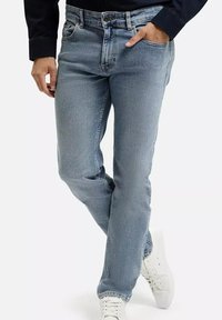 Jasnoniebieskie dżinsy o klasycznym kroju, z pięcioma kieszeniami i zapi�ęciem na guzik. Noszone z ciemną bluzką i białymi trampkami, ukazując detale w strukturze materiału.